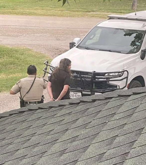 Ron Helms in handcuffs beside a patrol truck outside his home