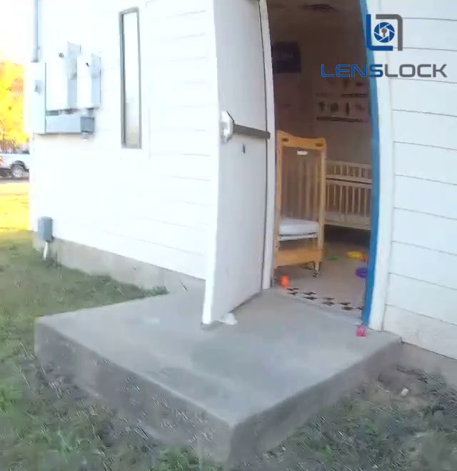The infant room's exit door at 4:49 p.m. on December 5, 2023, on the responding officer's body camera, about ten minutes before Stearman arrived. The stopper is the white object at the foot of the door. I can't tell from the video whether the stopper was there when the toddlers walked out. I cropped the frame to the door.